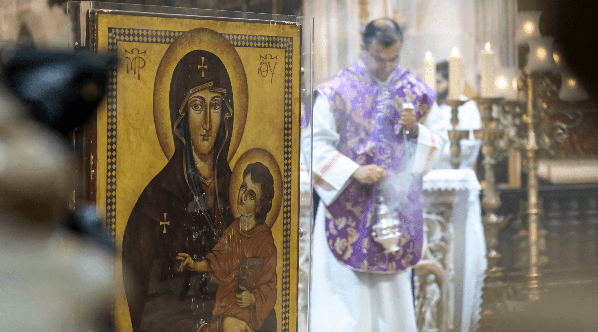 Ícone mariano em primeiro plano, com um Padre no decorrer da celebração de receção dos Símbolos, ao fundo, desfocado