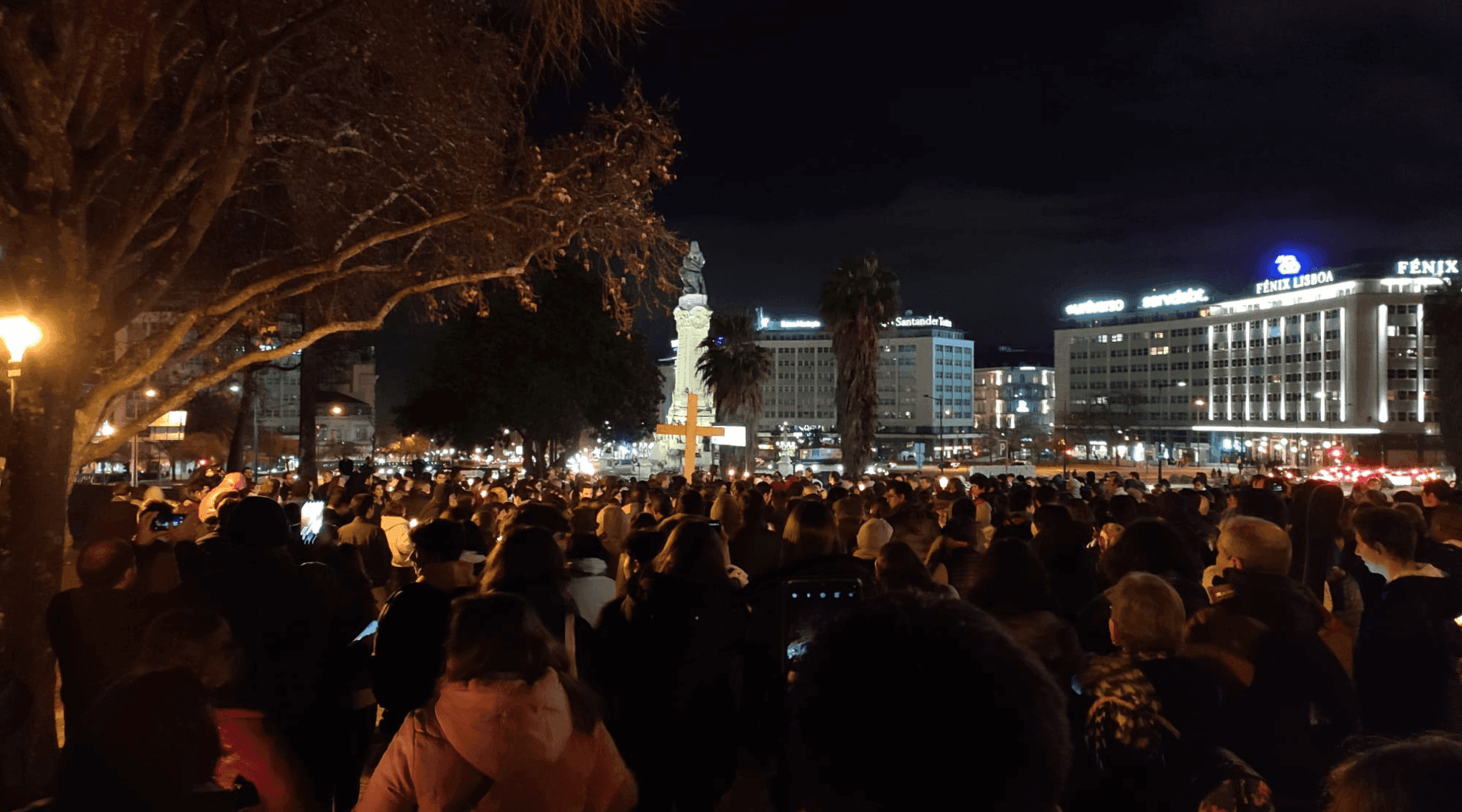 Multidão caminha atrás da Cruz. Em segundo plano, rotunda do Marques de Pombal iluminada