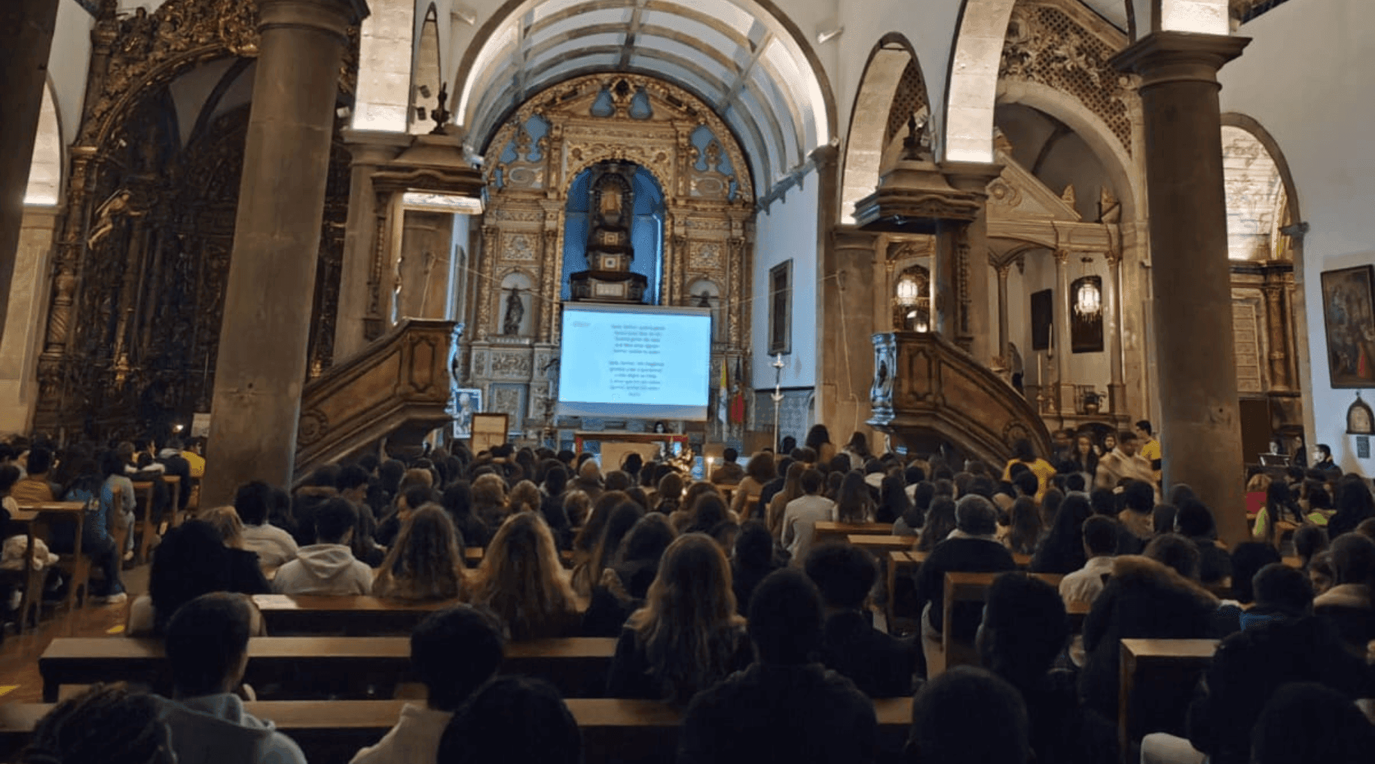 Fotografia abiente que mostra as pessoas sentadas na Igreja, a rezar em conjunto