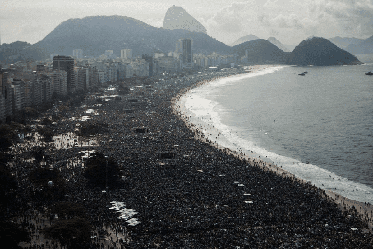 Multitud en la playa de Copacabana, con la playa de arena al fondo. Paisaje con el Pan de Azúcar detrás, el mar a la derecha y los edificios a la izquierda