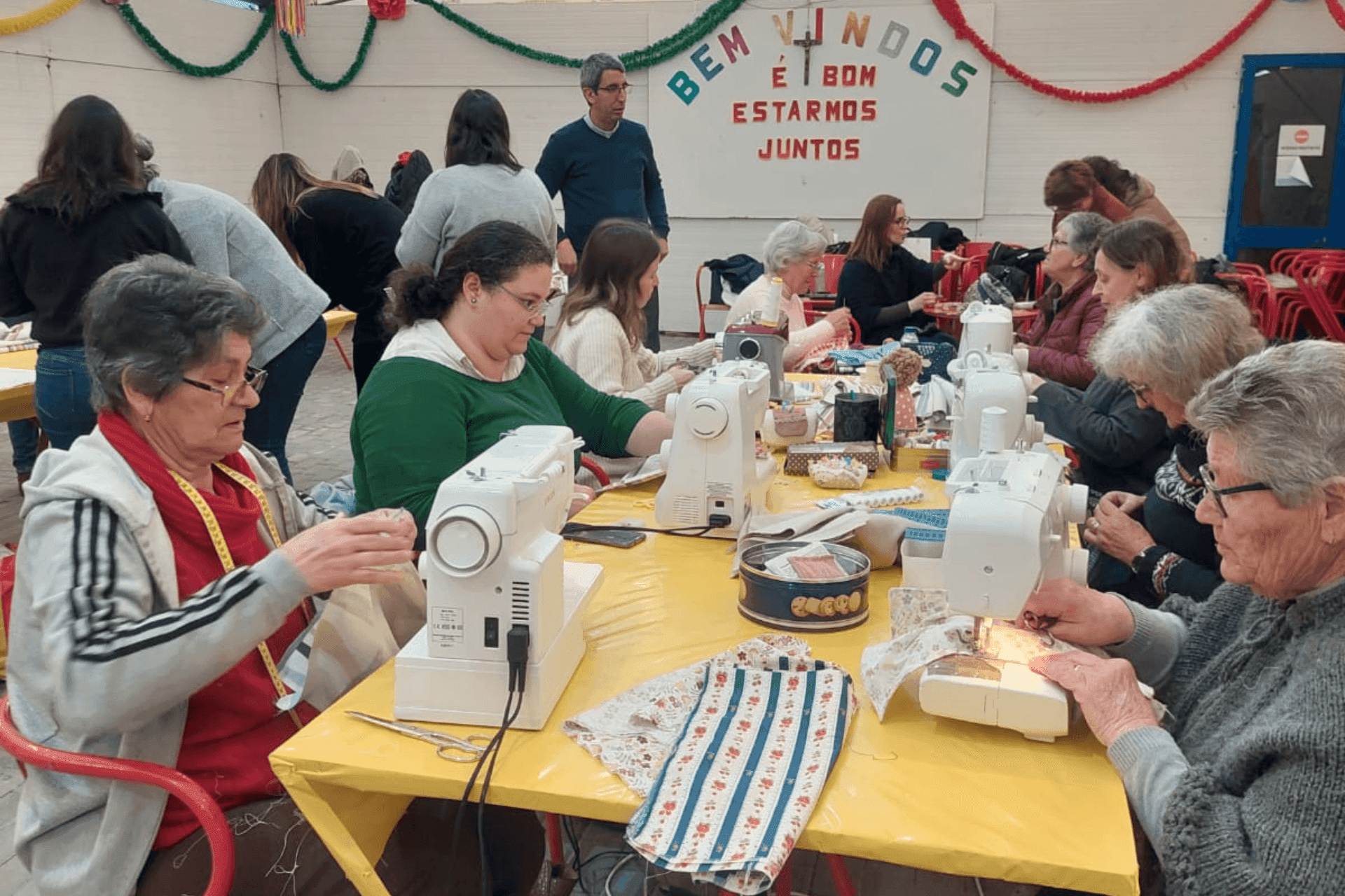 Pessoas de várias gerações a costurarem à máquina sacos de pano para os peregrinos da JMJ Lisboa 2023